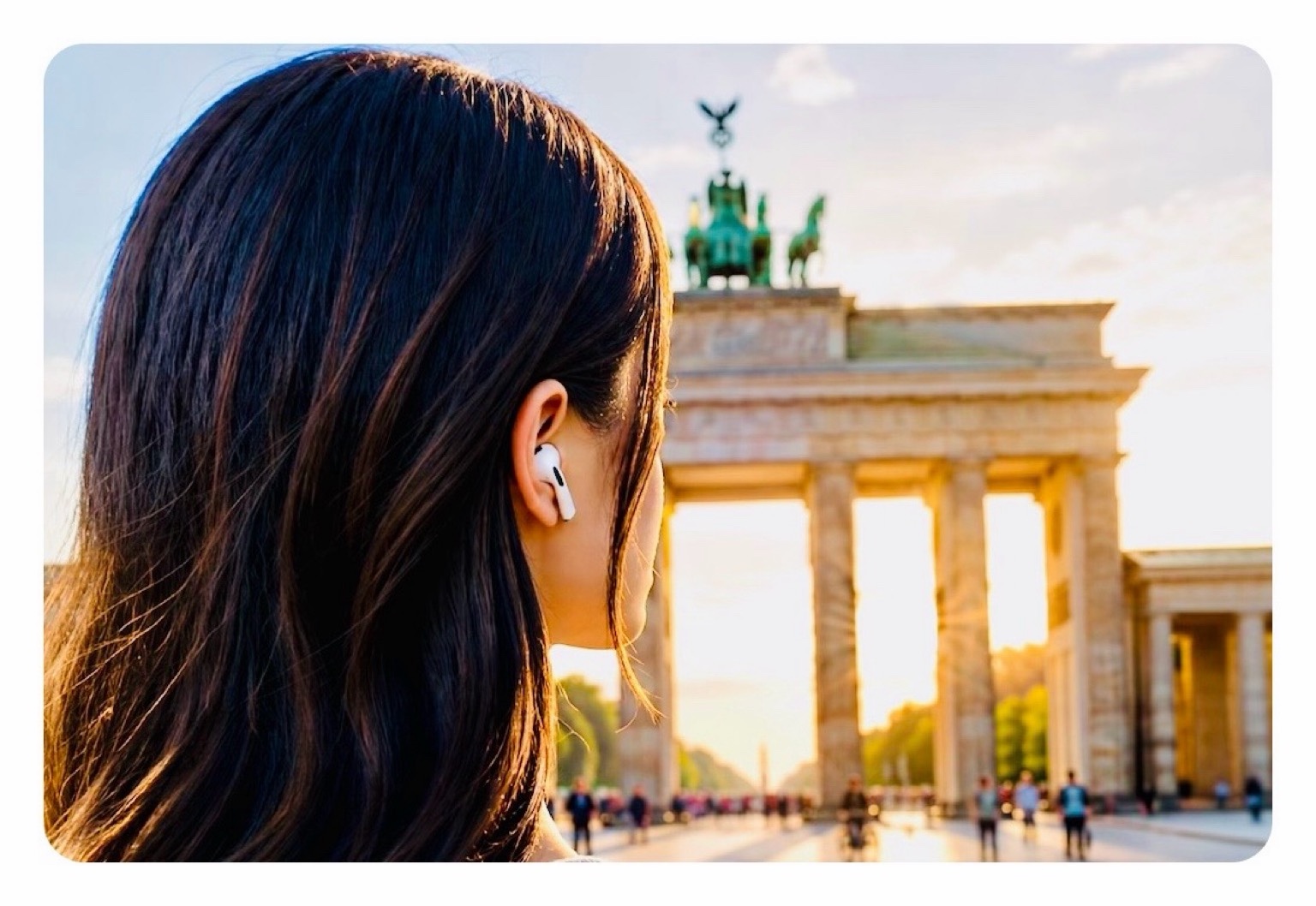 Titelbild: Zu sehen ist eine junge Frau mit dunklen, langen Haaren und AirPods in den Ohren, die gerade eine Sehenswürdigkeit bei einer Stadtführung besucht. 